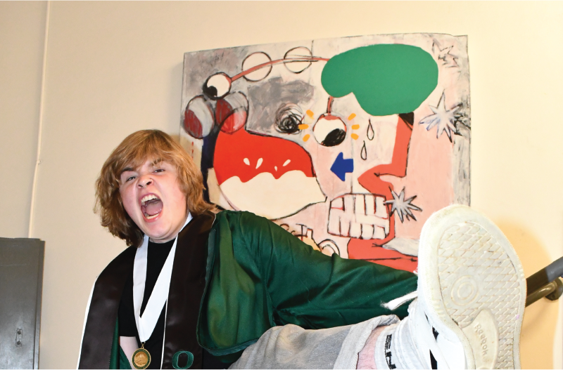 Maegan in graduation regalia kicking in front of the painting (very) nervous nervous system (2023)